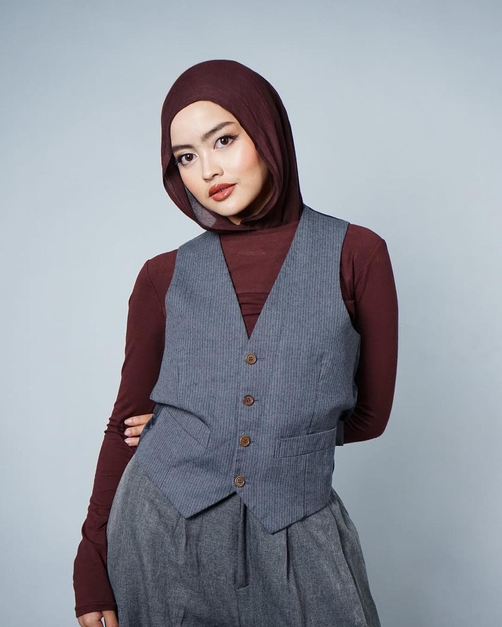 Model hijab fashion editorial dengan outfit maroon dan vest abu-abu
